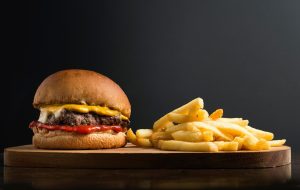 Cheeseburger con patatine fritte su tagliere di legno, sfondo scuro