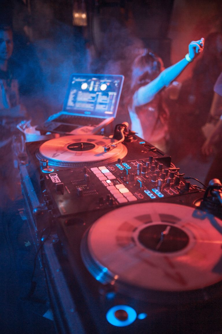 Consolle DJ con vinili in un locale con luci blu e rosse e persone che ballano