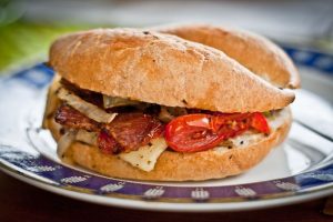 Panino gourmet con pancetta grigliata, formaggio, pomodori e cipolle su piatto